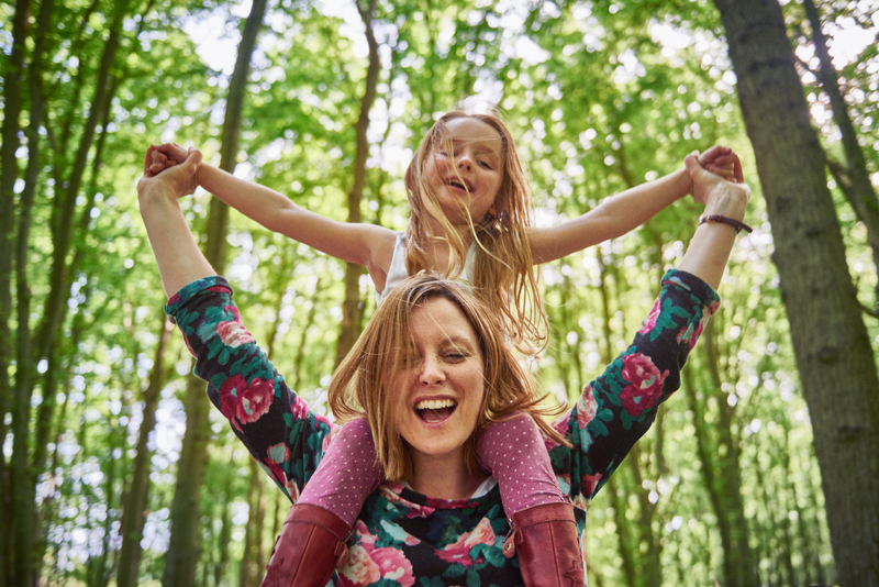 Woman giving daughter a shoulder ride in forest - Getty Images