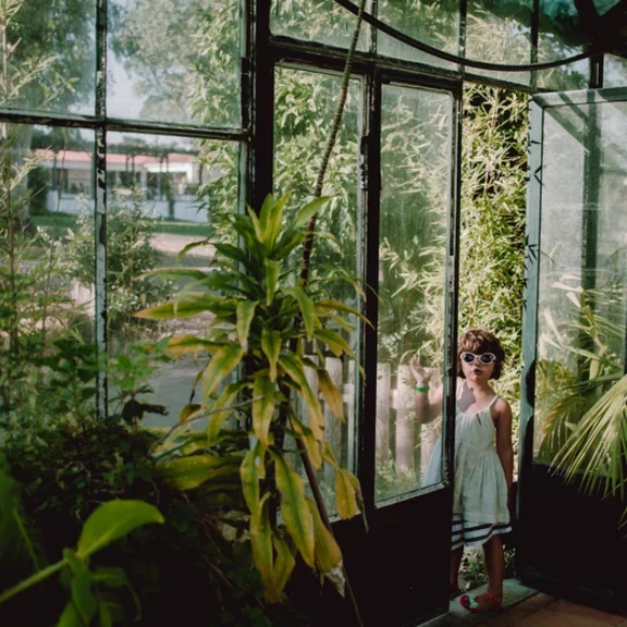 Girl wearing sunglasses standing near a greenhouse door